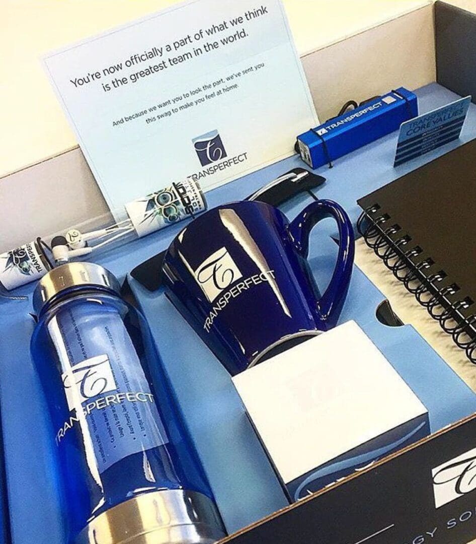 A blue and silver bottle, mug, note pad and pen on top of a desk.