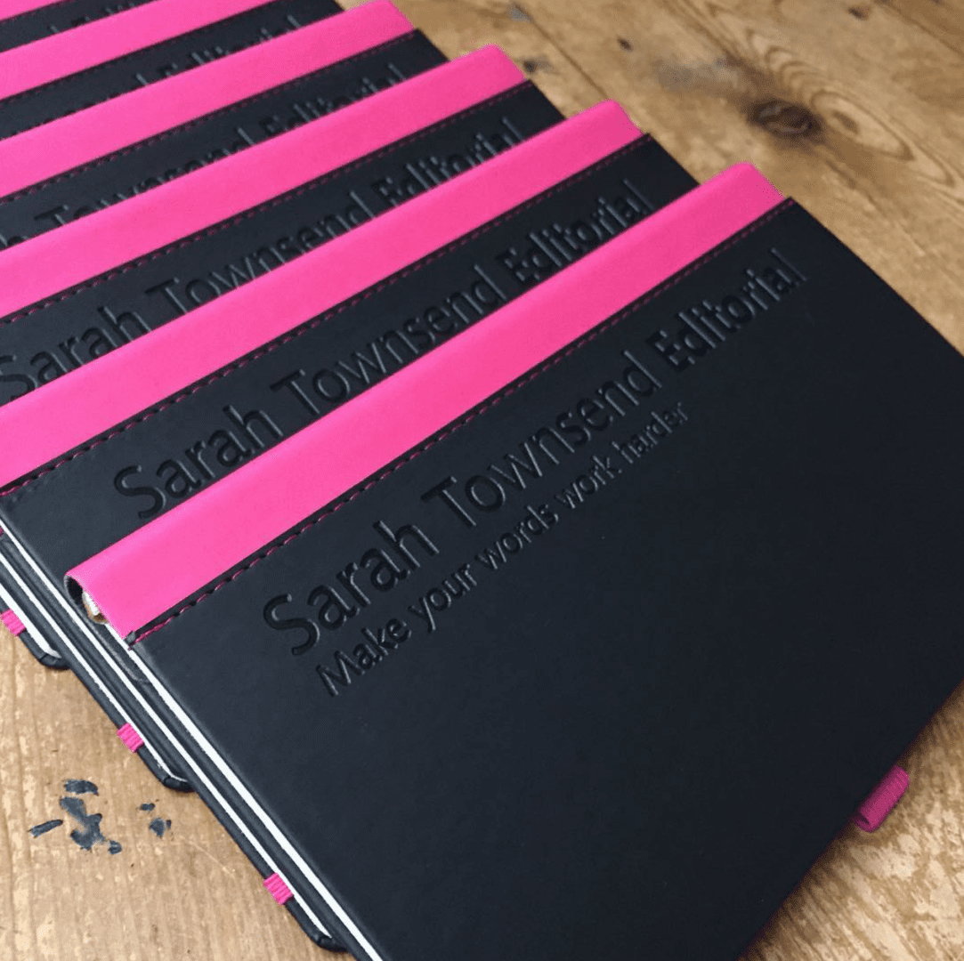 A group of pink and black books on top of a wooden table.