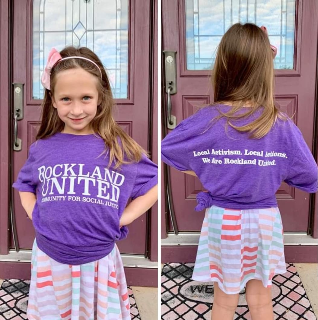 A girl in purple shirt and skirt standing next to door.